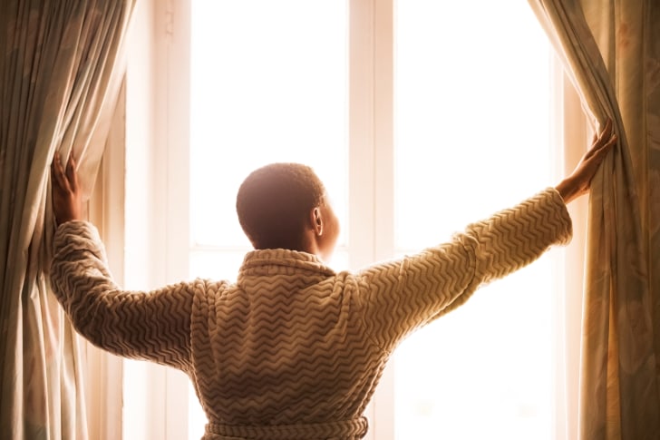 photo of a woman opening her curtains in the morning